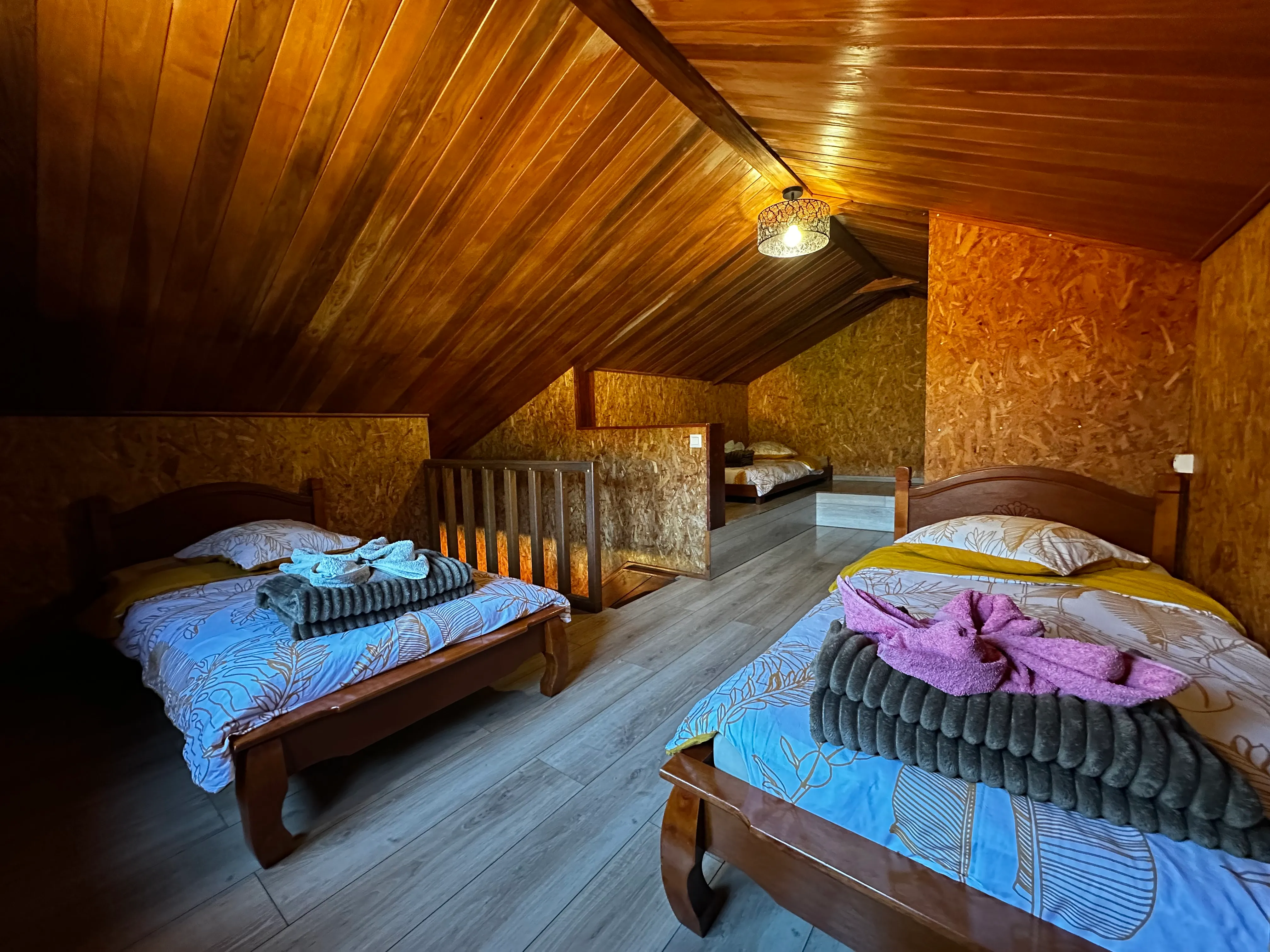 Dortoir 4 places sous les toits : lits simples en bois, serviettes pliées, charpente apparente